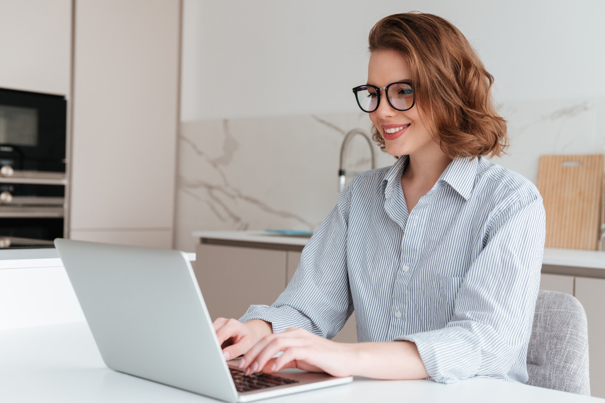 elegant-smiling-woman-glasses-striped-shirt-using-laptop-computer-while-siting-table-kitchen