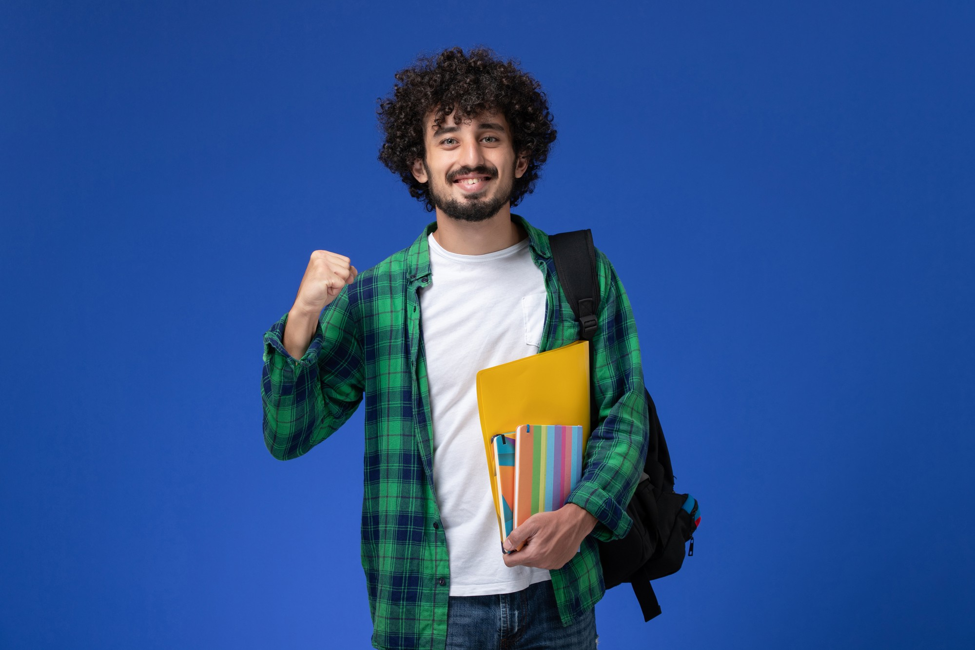 front-view-male-student-wearing-black-backpack-holding-copybooks-files-blue-wall