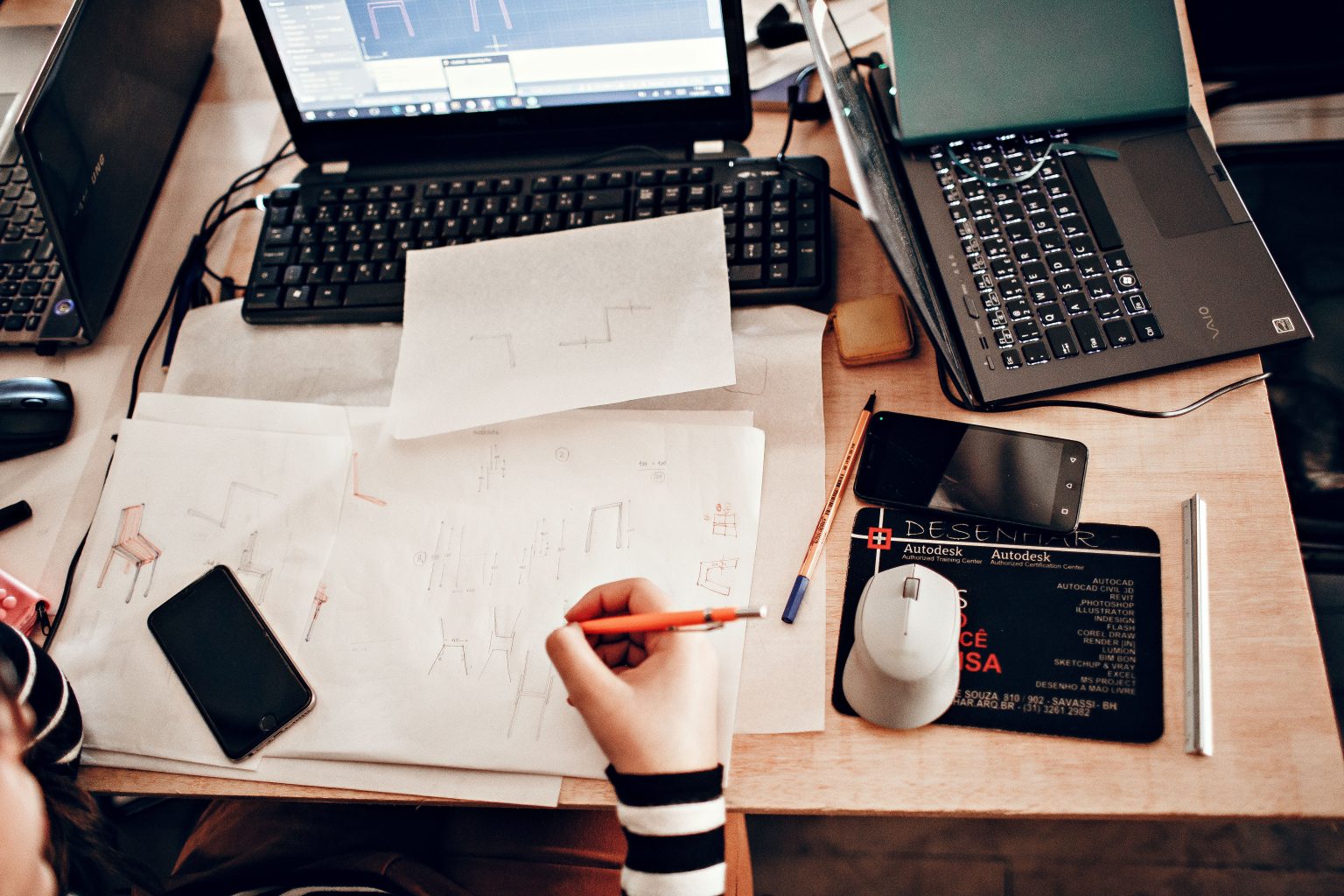 Pessoa desenha um projeto arquitetônico à mão enquanto utiliza ferramentas digitais de arquitetura.